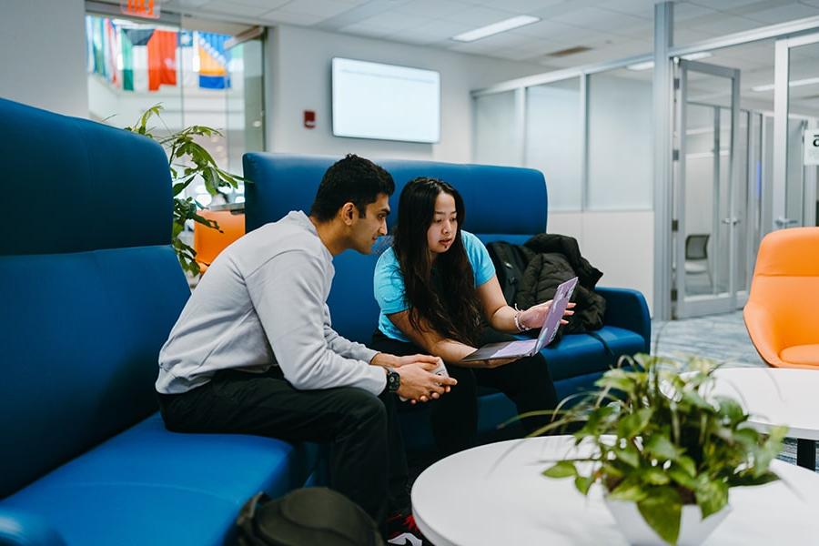 two students sit in couch in One Stop office looking at screen on laptop